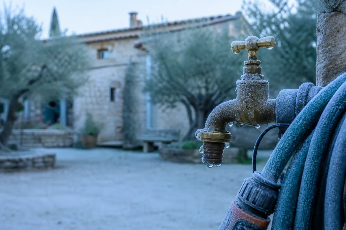 Robinet extérieur et tuyau d&rsquo;arrosage givrés le matin dans une cour de mas provençal