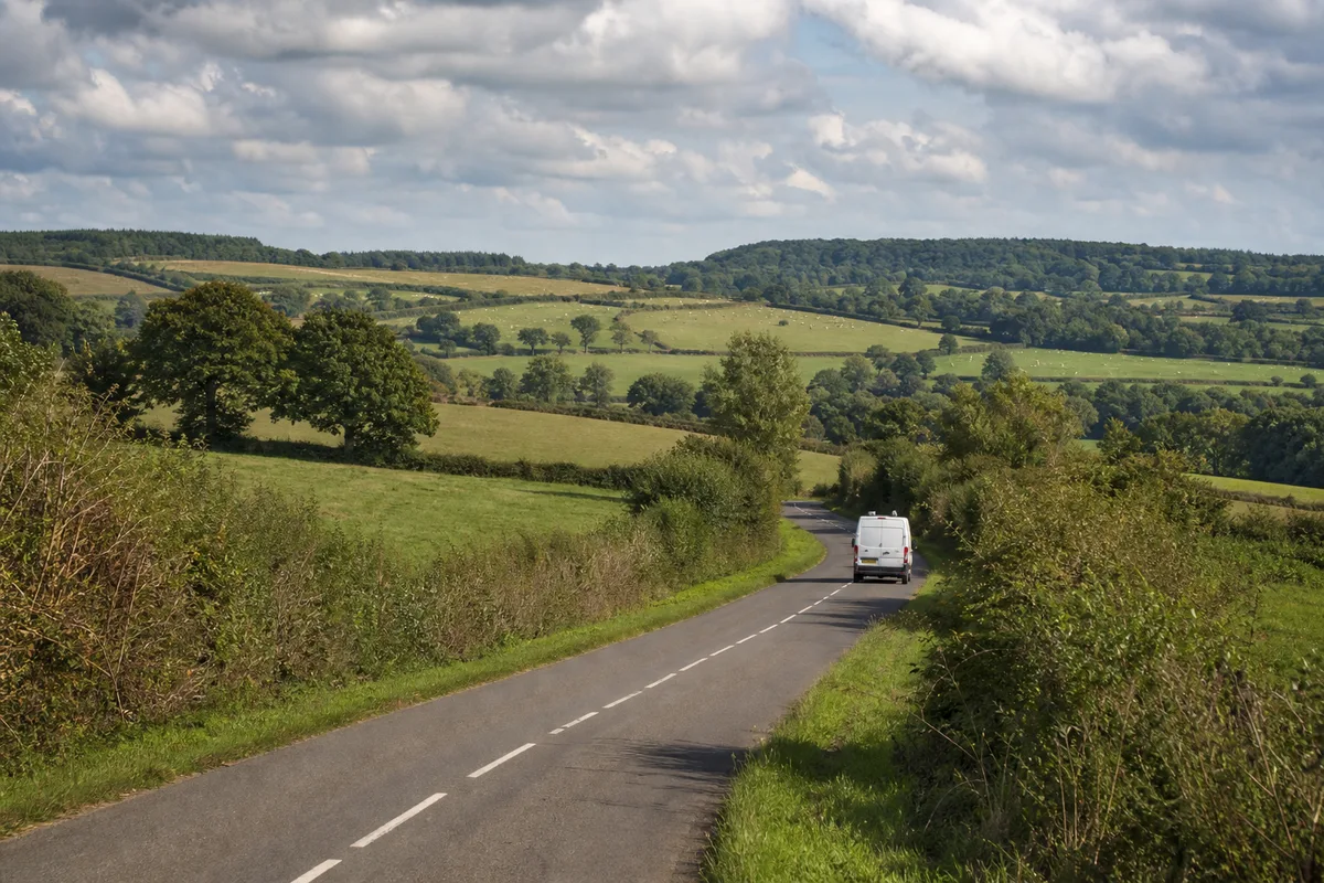 Camionnette d&rsquo;artisan plombier roulant sur une petite route bordée de haies bocagères normandes